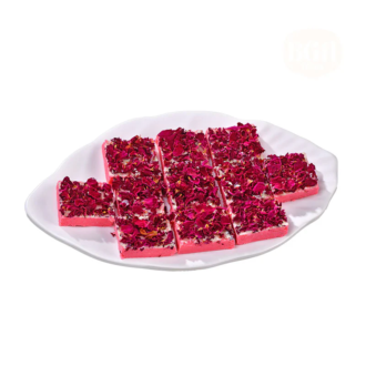 A white plate filled with square pieces of rose petal burfi, garnished with vibrant red edible rose petals, showcasing its creamy texture and elegant presentation.